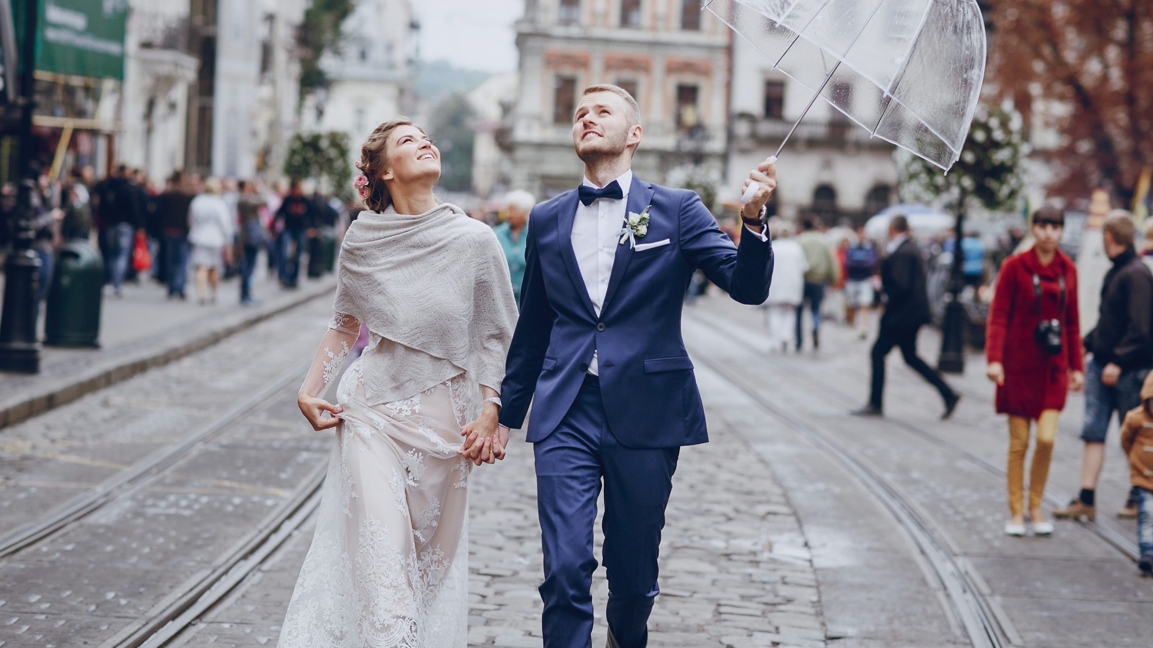 Frau und Mann stehen an ihrem Hochzeitstag im Regen und halten einen Schirm in der Hand.